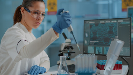 Chemist working on experiment with micro pipette and beaker, using dropper on test tube to develop...