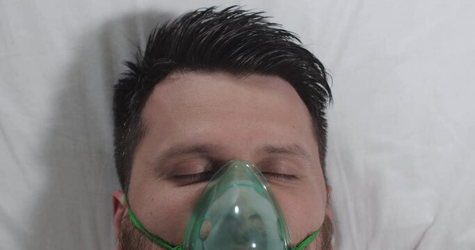 Close-up of a young man opening his eyes in a hospital bed in an intensive care unit. The patient comes out of a coma or wakes up after anesthesia.