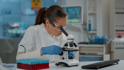 Portrait of scientist looking through microscopic lens in laboratory, working on experiment with...