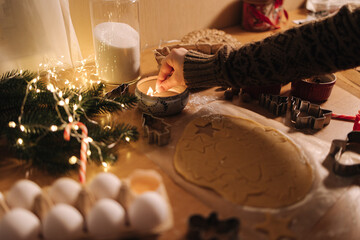 Naklejka na ściany i meble Woman lights a candle on Christmas. Preparing for baking gingerbread. Christmas mood