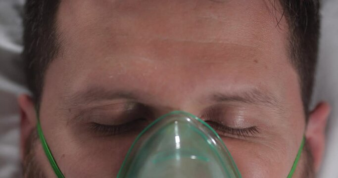 Extreme close-up of a young man opening his eyes in a hospital bed in an intensive care unit. The patient comes out of a coma or wakes up after anesthesia.