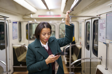 Businesswoman in subway carriage using smartphone to send business email or text with family. Young...