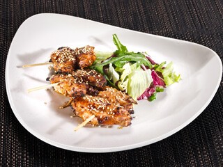 portion of grilled chicken wings skewers with mix salad on a plate on dark background