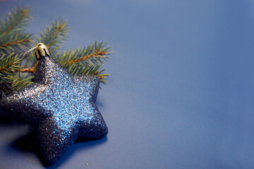 a shiny blue Christmas toy in the shape of a star stands next to a branch of a Christmas tree on a...