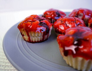 five gluten-free muffins with rice flour cherries sprinkled with cherries and red syrup stand on a gray plate on a white background. side view. homemade gluten-free cakes