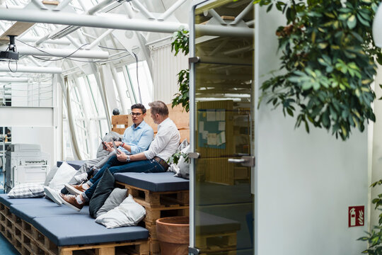 Male colleagues working while sitting on sofa at office