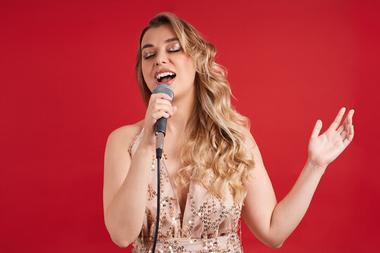 Lovely singer singing into a microphone, closing her eyes on a red background