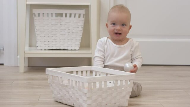 Baby sitting on the floor playing with plastic balls from toy storage basket, cute 9 month old baby boy having fun taking out ball from basket at hom. High quality 4k footage