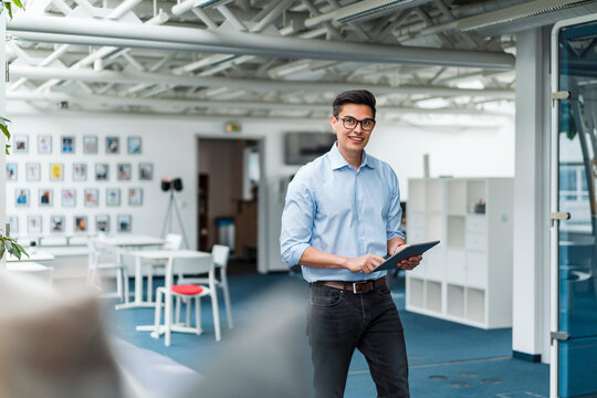 Smiling Businessman Holding Digital Tablet While Walking In Office