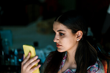 Young woman holding smart phone in dark room