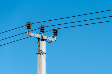 reinforced concrete pillar with high-voltage wires against a clear blue sky. Transmission of...