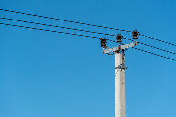 Obraz premium reinforced concrete pillar with high-voltage wires against a clear blue sky. Transmission of electricity by wires over long distances.