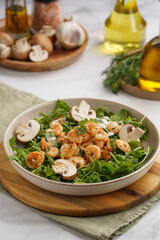 Arugula salad with shrimp and champignons, olive oil and dill on a wooden board on a white surface