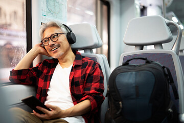 Senior man traveling by train. Man listening the music while enjoying in travel..