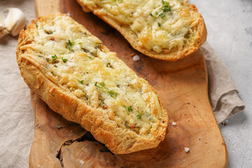 Two halves of garlic and butter bread - baguette on a wooden board, sea salt, pepper, dill and garlic cloves on a grey concrete background, top view