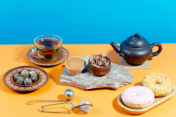 Tea in a cup in a composition with pastries and dessert, on a bright colored background.