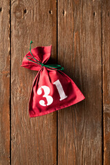 Red textile bag tied with green thread with date number thirty one on wooden background. Advent calendar, last pouch of December. Vertical photography, copy space.