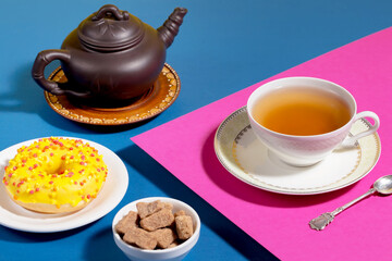 Tea in a cup in a composition with pastries and dessert, on a bright colored background.