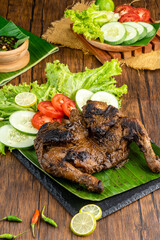Ayam bakar or roasted chicken on banana leaf shoot at a rustic wooden background. Ayam bakar is a indonesian dish. Ayam bakar literally means 