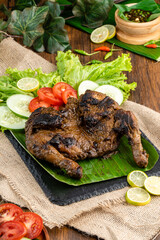 Ayam bakar or roasted chicken on banana leaf shoot at a rustic wooden background. Ayam bakar is a indonesian dish. Ayam bakar literally means 
