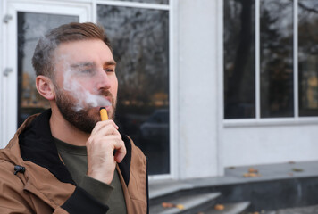 Handsome young man using disposable electronic cigarette outdoors