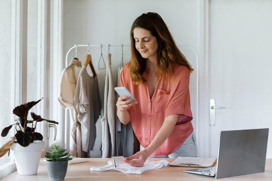 Smiling businesswoman taking photo of price tag through smart phone at home