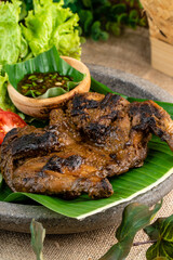 Ayam bakar or roasted chicken on banana leaf shoot at a rustic wooden background. Ayam bakar is a indonesian dish. Ayam bakar literally means 