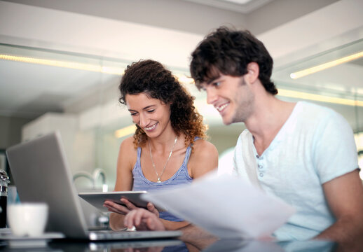 Smiling man using laptop while holding document by girlfriend in kitchen