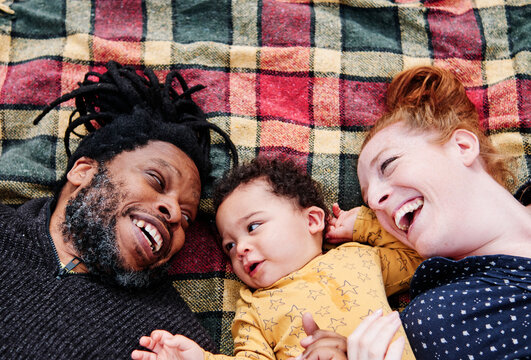 Cheerful family relaxing with son while lying on picnic blanket at park
