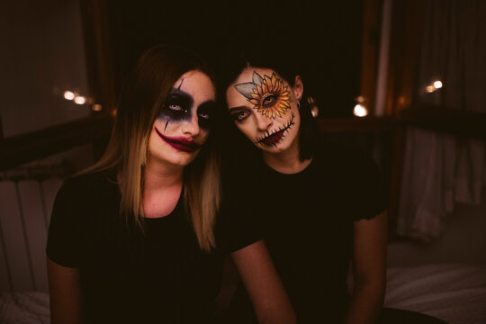 Female friends with Halloween make-up sitting on bed at home
