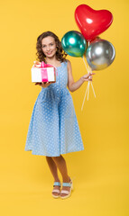 studio, beautiful woman. model on a yellow background in a blue dress holds balls, has fun in the camera. model pose. photo session, holiday. birthday