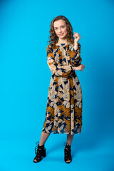 studio, beautiful woman. model on a blue background in a dark blue dress with a yellow floral armenite poses for the camera. model pose. beauty shooting, holiday