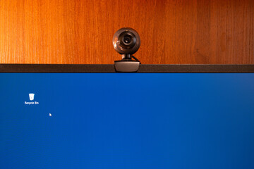 External round black web camera on a black monitor blue screen. Webcam on a wooden background.