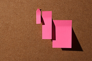 Pink square office sticky notes on cork board with hard shadow