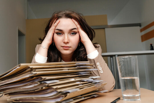 Tired young businesswoman sitting with hand in hair at desk in office