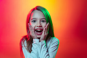 Portrait of surprised little girl, happy kid looking at camera with open mouth isolated on red...