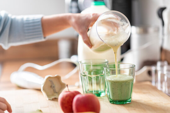 Woman Pouring Smoothie In Glass On Kitchen Counter