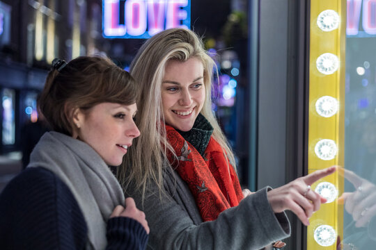 Smiling young women doing window shopping together at night