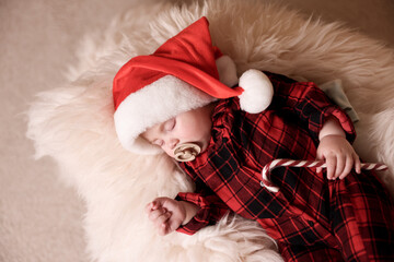 Fototapeta premium Cute baby in Santa hat with candy cane sleeping on soft faux fur, top view. Christmas season