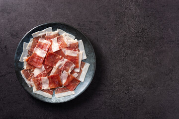 Spanish serrano ham slices on black plate on black background. Top view. Copy space