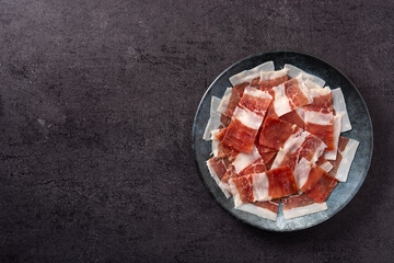 Spanish serrano ham slices on black plate on black background. Top view. Copy space
