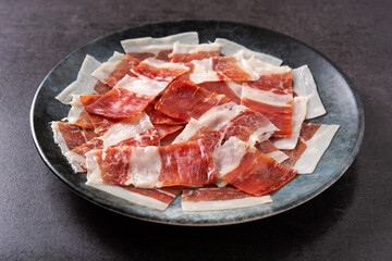 Spanish serrano ham slices on black plate on black background