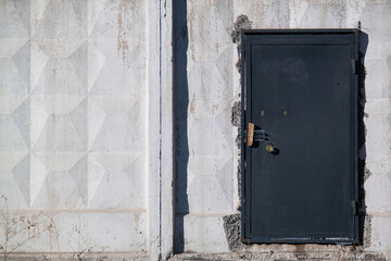 A black abandoned metal door in the white concrete wall