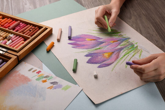 Woman drawing beautiful crocus flowers with soft pastel at wooden table, closeup