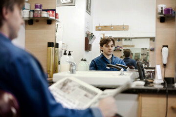 Reflection of barber reading newspaper in barber shop