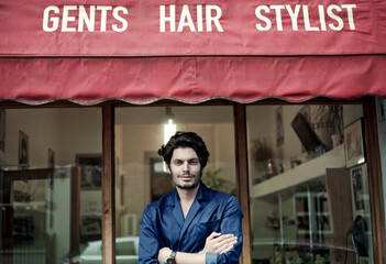 Portrait of handsome barber standing in front of barber shop with crossed arms