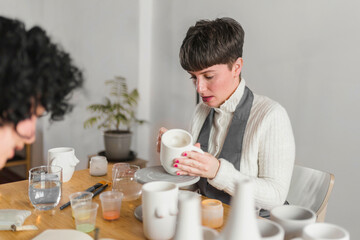 Female artisanal checking cup while working with colleague at workplace