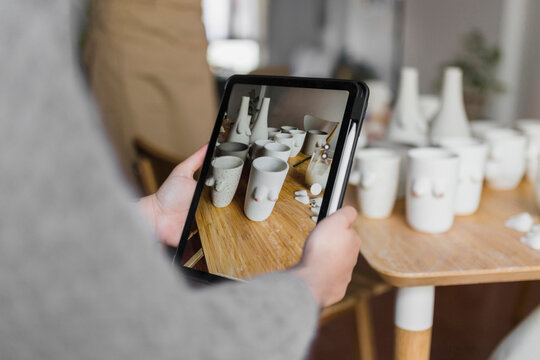 Female artist photographing art products through digital tablet at workshop