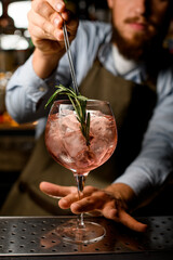 selective focus on rosemary branch of which the bartender decorates goblet glass with drink