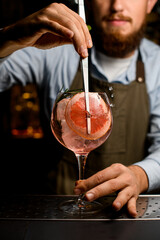 Fototapeta na wymiar goblet glass with cold cocktail that the hand of barman decorating by fresh slice of grapefruit using tweezers